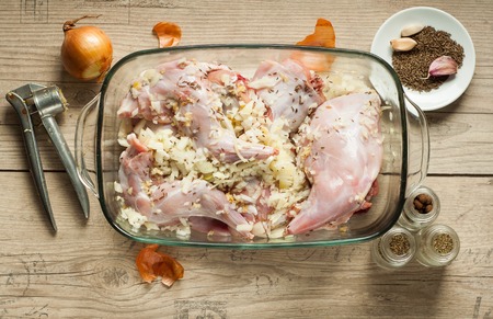 raw rabbit meat in roaster with onion cumin and garlic on wooden vintage tableの写真素材