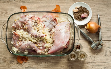 raw rabbit meat in roaster with onion cumin and garlic on wooden vintage tableの写真素材