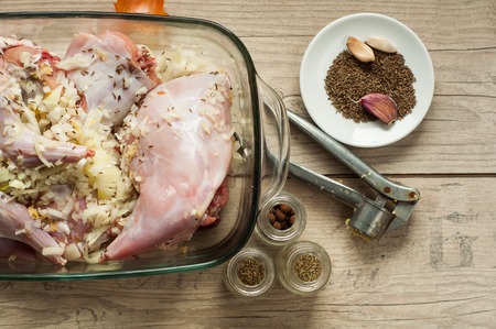 raw rabbit meat in roaster with onion cumin and garlic on wooden vintage tableの写真素材