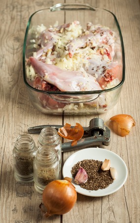 raw rabbit meat in roaster with onion cumin and garlic on wooden vintage tableの写真素材