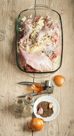 raw rabbit meat in roaster with onion cumin and garlic on wooden vintage tableの写真素材