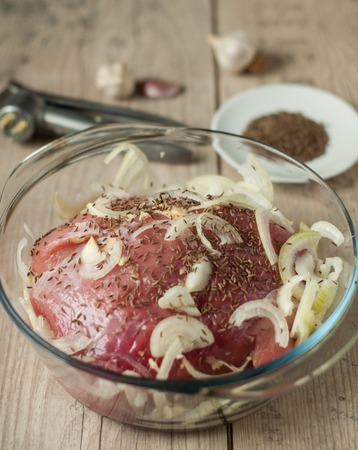 raw pork meat in roaster with onion cumin and garlic on wooden tableの写真素材