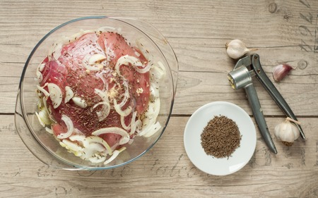raw pork meat in roaster with onion cumin and garlic on wooden tableの写真素材