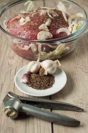 raw pork meat in roaster with onion cumin and garlic on wooden tableの写真素材