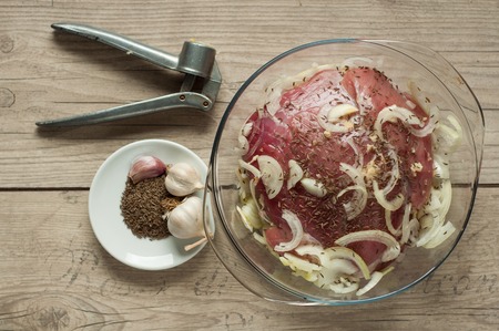 raw pork meat in roaster with onion cumin and garlic on wooden tableの写真素材
