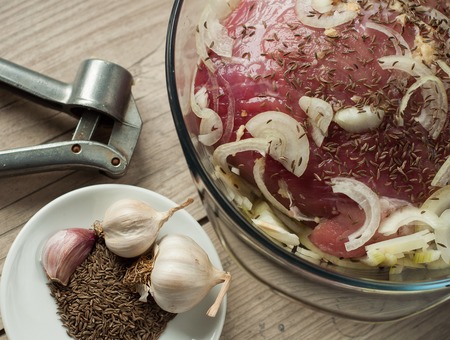raw pork meat in roaster with onion cumin and garlic on wooden tableの写真素材