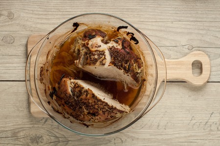baked pork meat in roaster with onion cumin and garlic on wooden tableの写真素材
