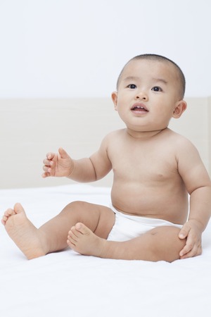 Cute Chinese baby boy sitting in bed, shot in Beijing, Chinaの写真素材
