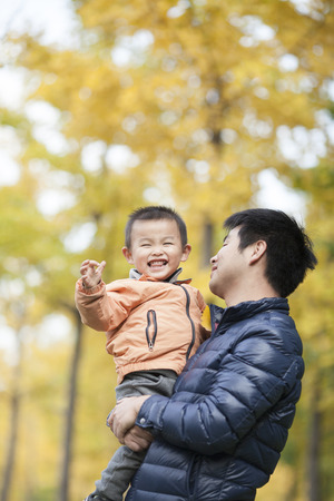 Happy real father and son playing in front of ginkgo trees, shot in Beijing, Chinaの写真素材