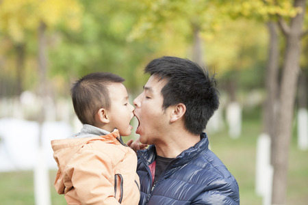 Happy real father and son playing in front of ginkgo trees, shot in Beijing, Chinaの写真素材