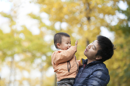 Happy real father and son playing in front of ginkgo trees, shot in Beijing, Chinaの写真素材