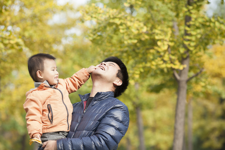 Happy real father and son playing in front of ginkgo trees, shot in Beijing, Chinaの写真素材