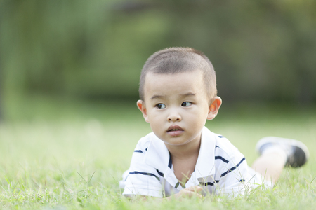 Happy Chinese baby boy lying on meadow, shot in Beijing, Chinaの写真素材