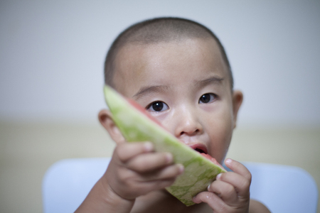 Happy Chinese baby boy eating watermelon indoors, Beijing, Chinaの写真素材