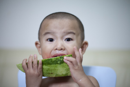 Happy Chinese baby boy eating watermelon indoors, Beijing, Chinaの写真素材