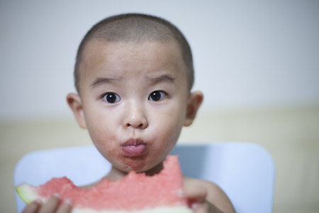 Happy Chinese baby boy eating watermelon indoors, Beijing, Chinaの写真素材