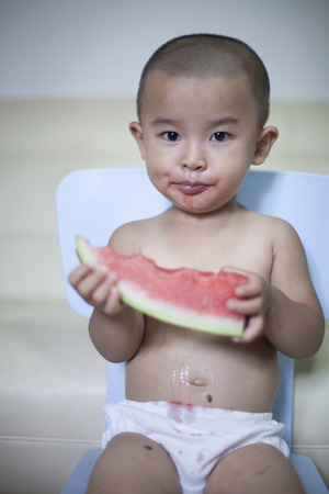 Happy Chinese baby boy eating watermelon indoors, Beijing, Chinaの写真素材