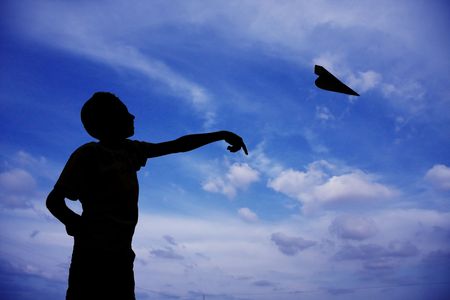 silhouette of a kid playing with a small plane with blue cloudy sky at the background の写真素材