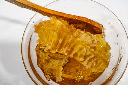honeycomb honey in glass bowl with wooden spoonの写真素材