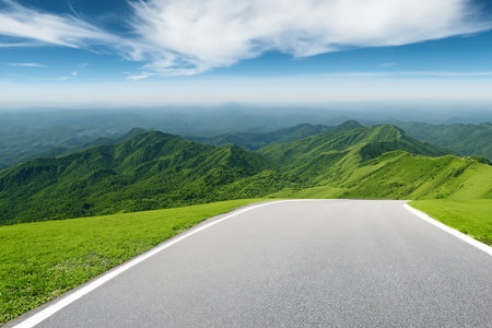 Asphalt road and green mountains under blue sky with white clouds.の素材
