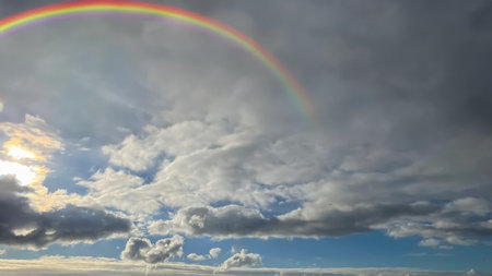 Rainbow in the sky with clouds and sun in the background.の素材