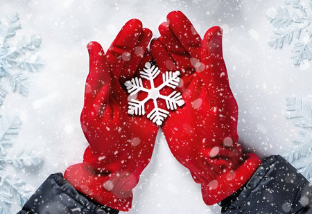 Hands in red gloves holding snowflake on white background with snowflakesの素材