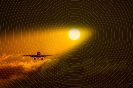 Silhouette of airplane flying into sunset sky with clouds and glowing sun. Airplane Silhouette at Sunset Sky with Glowing Sun and Clouds.の写真素材