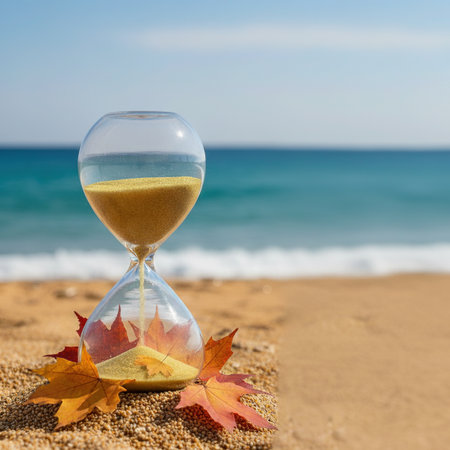 Sandglass with autumn leaves on a sandy beach against the background of the seaの素材