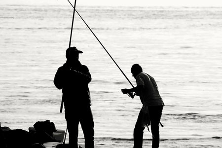 Silhouette of fishermen fishing on the beach at sunset. Black and white.の写真素材