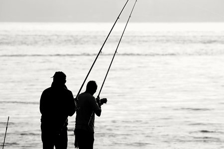 Silhouette of two fishermen with fishing rods on the beach.の写真素材