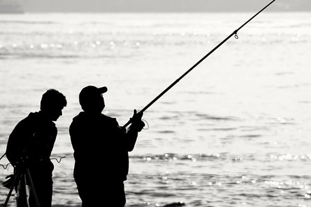 Silhouette of two fishermen on the beach at sunset. Black and white photo.の写真素材