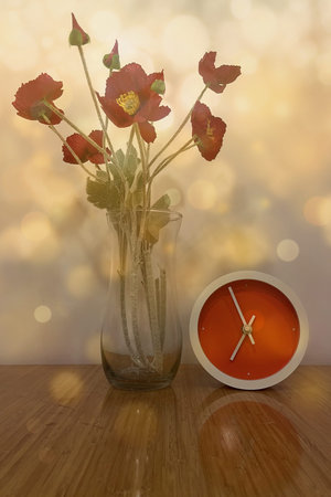 Red poppies in vase with alarm clock on wooden table