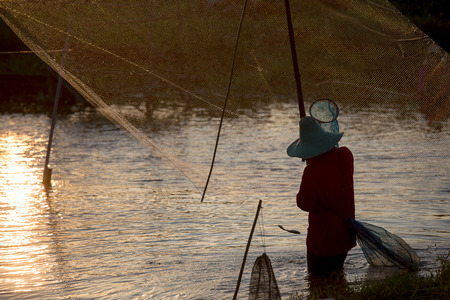 The Asian fisherman’s fishing at the lake by his equipment with rural scene.