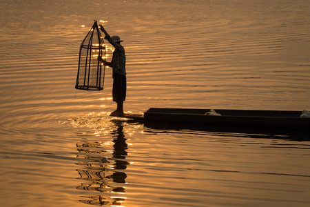 The Asian fishermanâ€™s fishing for fishes on his boat by his equipment at the lake.