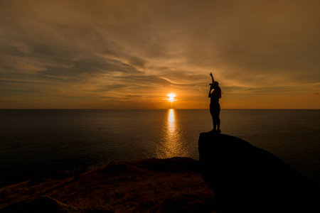 silhouette of man sit on rock in sunset.の写真素材