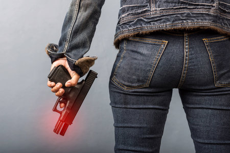 Woman in jeans is holding a gun in her hand with light effect.の写真素材