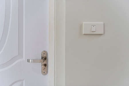 White lighting switches on wall and door handle on wall at home.