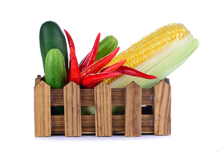 Fresh raw corn and fresh cucumbers and chili pepper in a wooden crate isolated  on white background.の写真素材