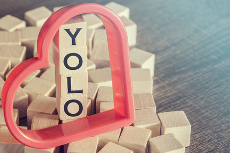 You Only Live Once YOLO message written with wooden blocks on a wooden table. Image cross processed for retro lookの写真素材