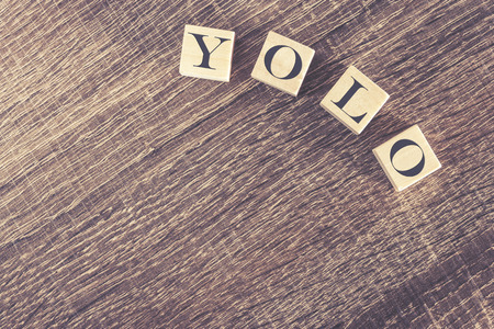 You Only Live Once YOLO message written with wooden blocks on a wooden table. Image cross processed for retro lookの写真素材