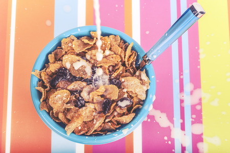Milk pouring on a bowl of cereals on a colorful kitchen table. Cross processed image with shallow...