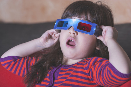 Little girl reacts while watching a 3D movie. Vintage effect image with shallow depth of fieldの写真素材