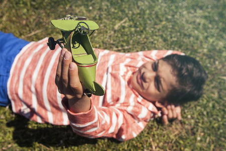 Boy holding a toy airplane lying on the grass