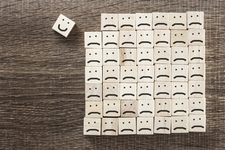 Positive attitude concept with wooden blocks. Smiling face standing out from the sad crowdの写真素材