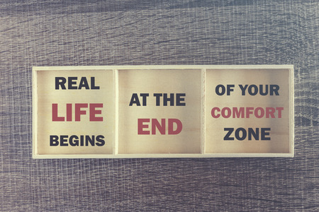 Real life begins at the end of your comfort zone. Inspirational quote written on wooden boxの写真素材