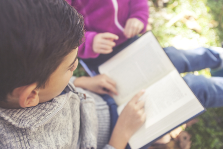 Kids reading a book outdoors.の写真素材