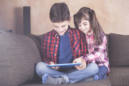 Brother and sister having fun with their tablet at home. Kids and technology conceptの写真素材
