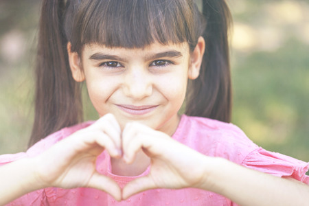 Love and childhood concept. Cute little girl making a heart shape with her handsの写真素材