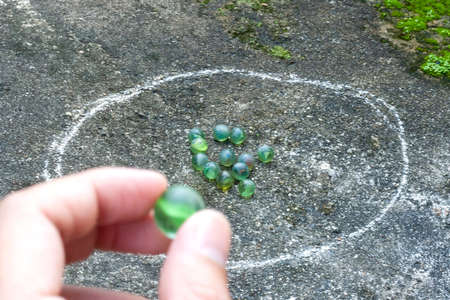 Close-up image of boy's hand playing marbles on the asphalt road.