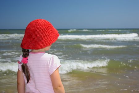 Girl in a red straw hat looking at the seaの写真素材